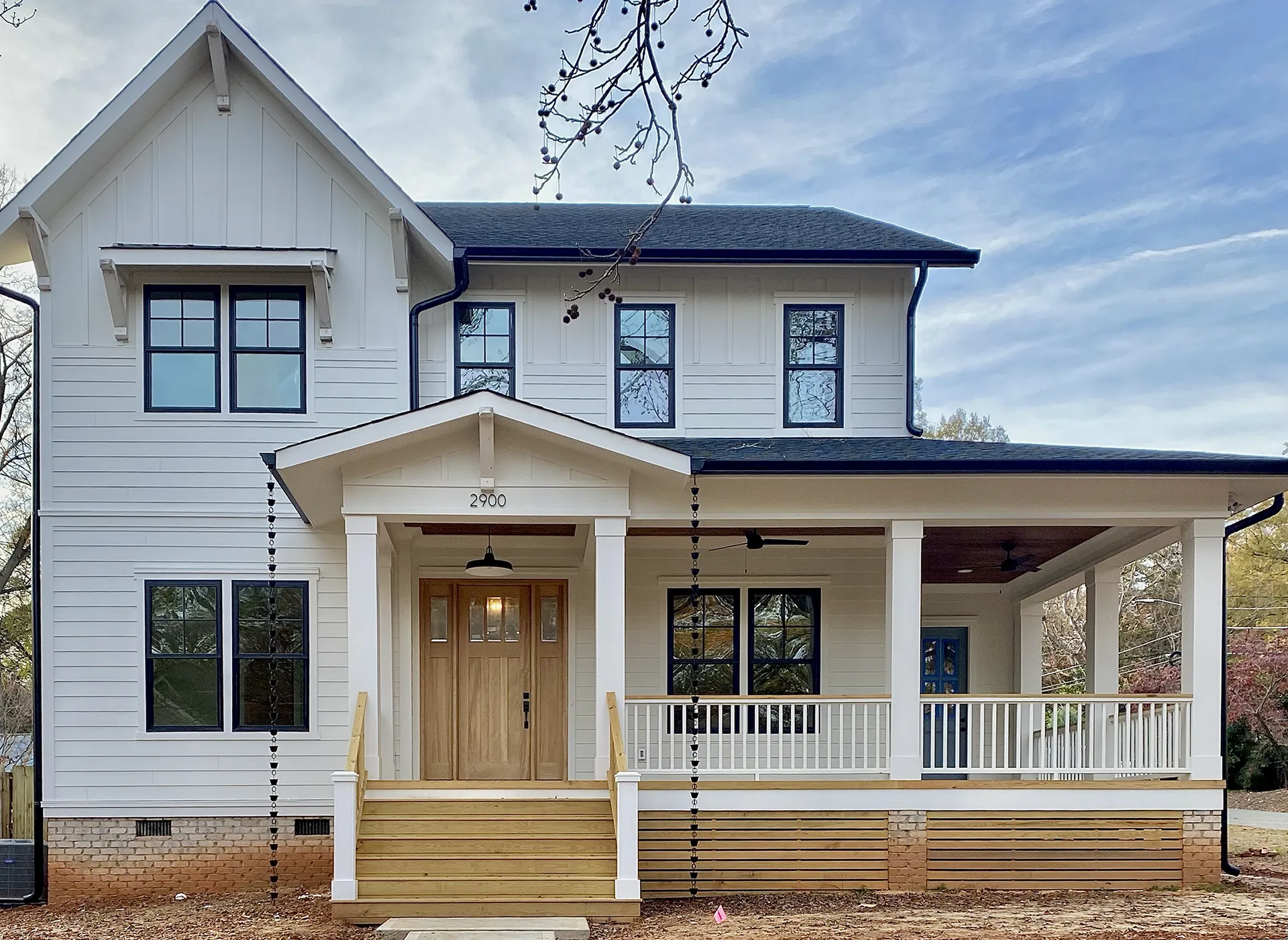 A two-story white house with black trim and a covered front porch featuring wooden steps and white railings.