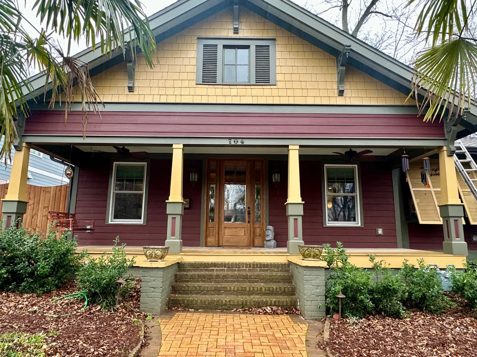 A charming bungalow with yellow and maroon siding, a covered porch, and a brick walkway leading to the entrance.